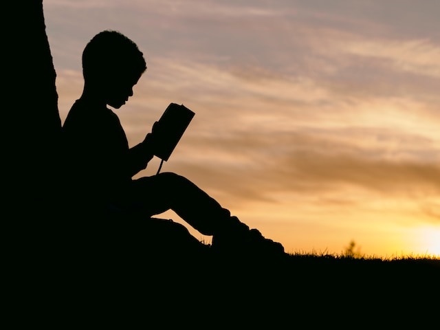 Image of a child reading a book. Education is about developing a child in every way. Photo by Aaron Burden on Unsplash
