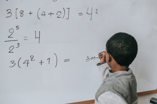 Education: Definition, What is Education? and Meaning. Education is all about empowering a child for future sustainability. A photo of a motivated male child solving a math problem on whiteboard. Photo by Katerina Holmes: https://www.pexels.com/photo/concentrated-black-kid-doing-sums-5905857/