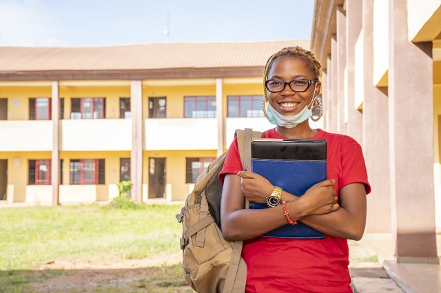 Private Institutions' Scholarship Images/Photos: 3. A photo of a student on scholarship standing in front of a private institution. Photo credit: wirestock on Freepik. https://www.freepik.com/free-photo/young-african-female-student-with-facemask-holding-her-textbooks-campus-area_16226448.htm#