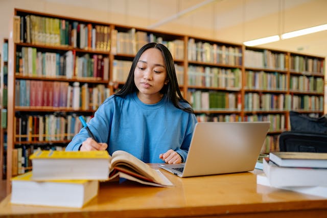 University College Scholarships Images/Photos: 3. A photo of a student on a research work in a higher education institution library. Photo by Yan Krukau: https://www.pexels.com/photo/woman-in-blue-long-sleeve-shirt-sitting-at-the-table-writing-8199557/