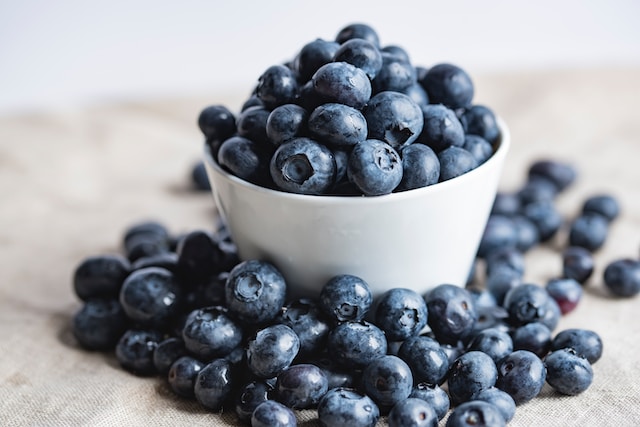 Fresh blueberries in a white bowl, scattered on a linen cloth. Part of 5 Best Healthy Fruits to Eat Everyday for their nutritional values and health benefits.