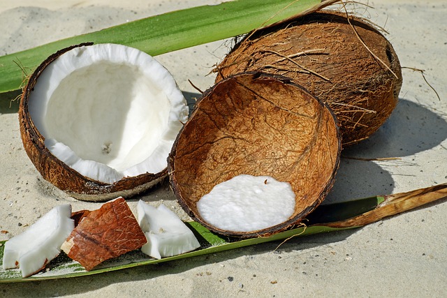 Whole and halved coconuts with white flesh and coconut pieces on a sandy background. Highlighted as one of the 5 Best Healthy Fruits for its nutritional values and health benefits.