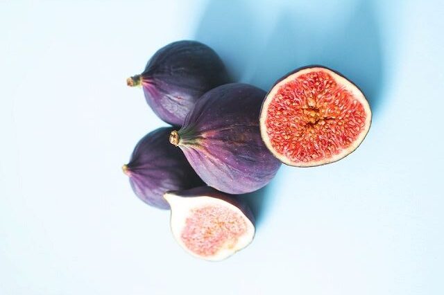 Whole and halved figs displaying deep purple skin and bright red-pink interior, set against a light blue background. Highlighted as one of the 5 Best Healthy Fruits to Eat Everyday for its nutritional values.