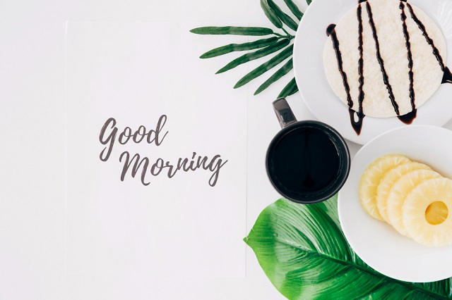 Free photo pineapple slices; tortillas and coffee on leaves with good morning text on paper over a white background