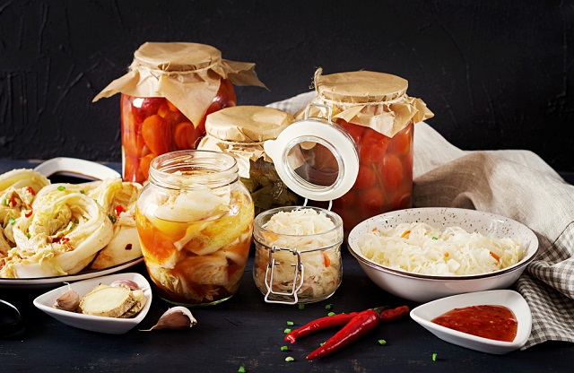 'What are Probiotics': Image cabbage kimchi, tomatoes marinated, sauerkraut sour glass jars over rustic kitchen table.